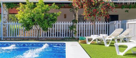 A swimming pool with a white fence and lounge chairs.