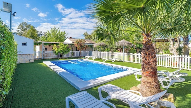 A rectangular swimming pool surrounded by artificial grass, white lounge chairs, and a white picket fence. - PaperoDor Prado del Rey by Ruralidays (Cádiz)