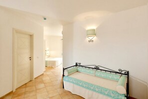 A bedroom with a bed, a door, a wall-mounted light, and a tiled floor.