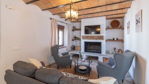 Una sala de estar con chimenea, dos sillones grises, un sofá y una mesa de centro con una botella y vasos.