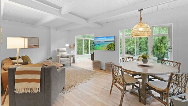 A spacious living area with a sofa, a dining table, and a TV mounted on the wall.