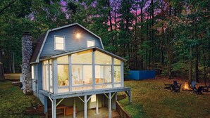 A cabin with a deck, a stone chimney, and a fire pit in the yard.