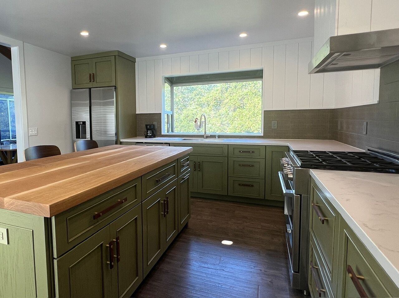 A kitchen with green cabinets, a wooden countertop, a window with a view, and a stove.