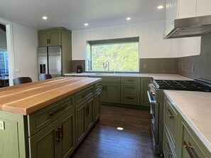 A kitchen with green cabinets, a wooden countertop, a window with a view, and a stove.