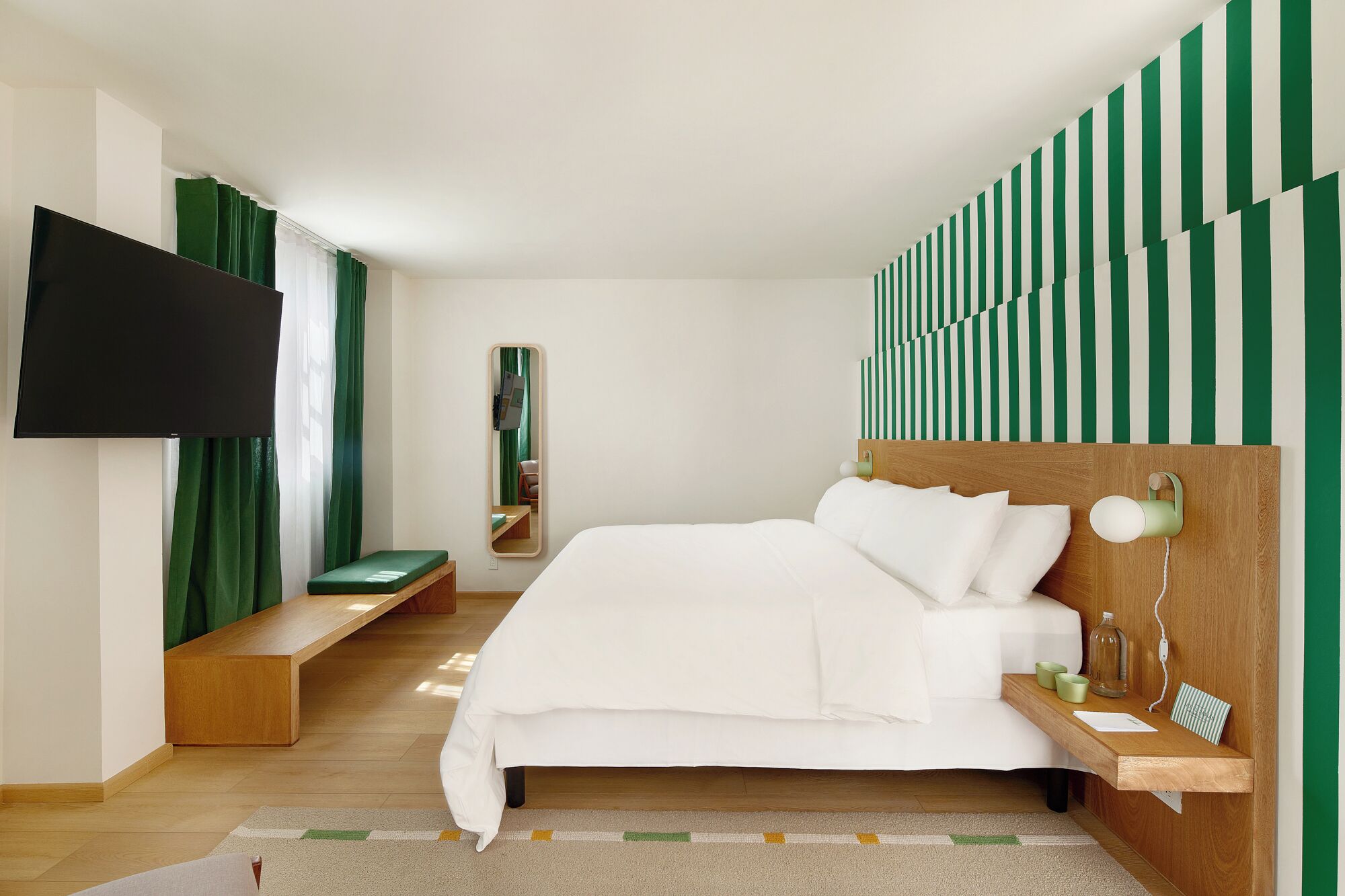 A modern hotel room with a large bed, a TV mounted on the wall, and a green-striped wall design.