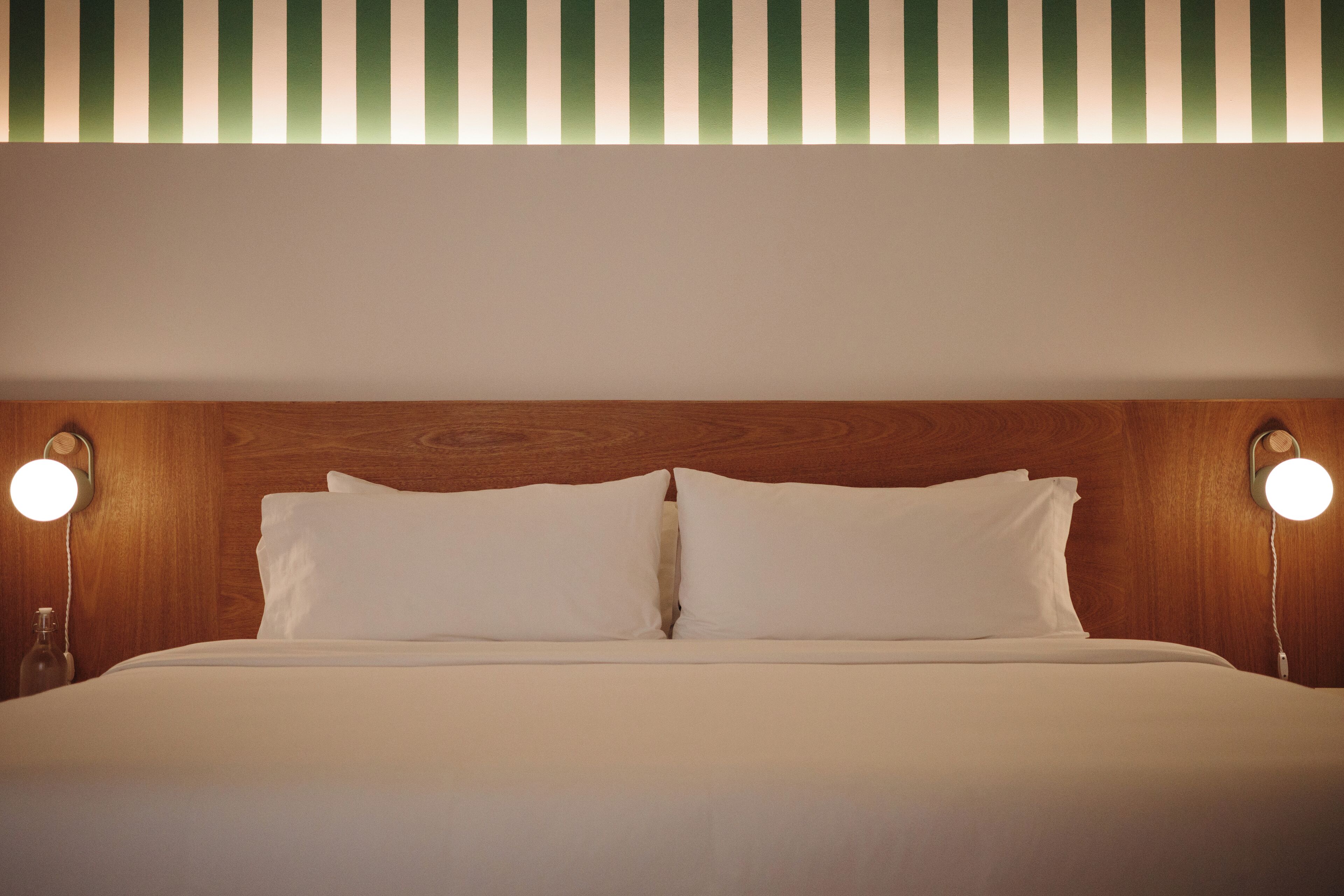 Una habitación de hotel con cabecera de madera, dos lámparas de noche y techo a rayas.