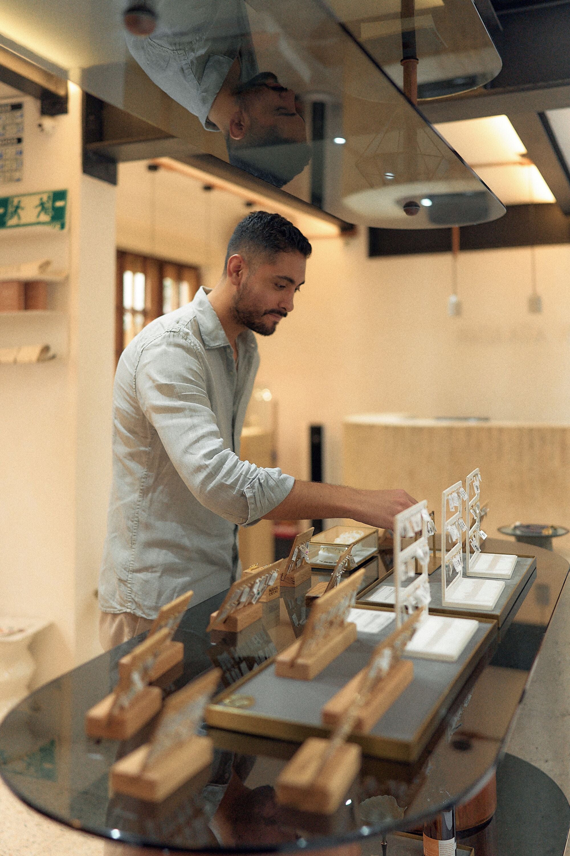 Une personne dispose des objets sur une table en verre dans un intérieur moderne agrémenté d’éléments en bois et où l’on peut voir une signalisation indiquant la sortie de secours.