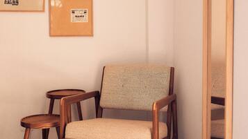 Una habitación con una silla de madera, una mesita redonda pequeña y dos objetos enmarcados en la pared.