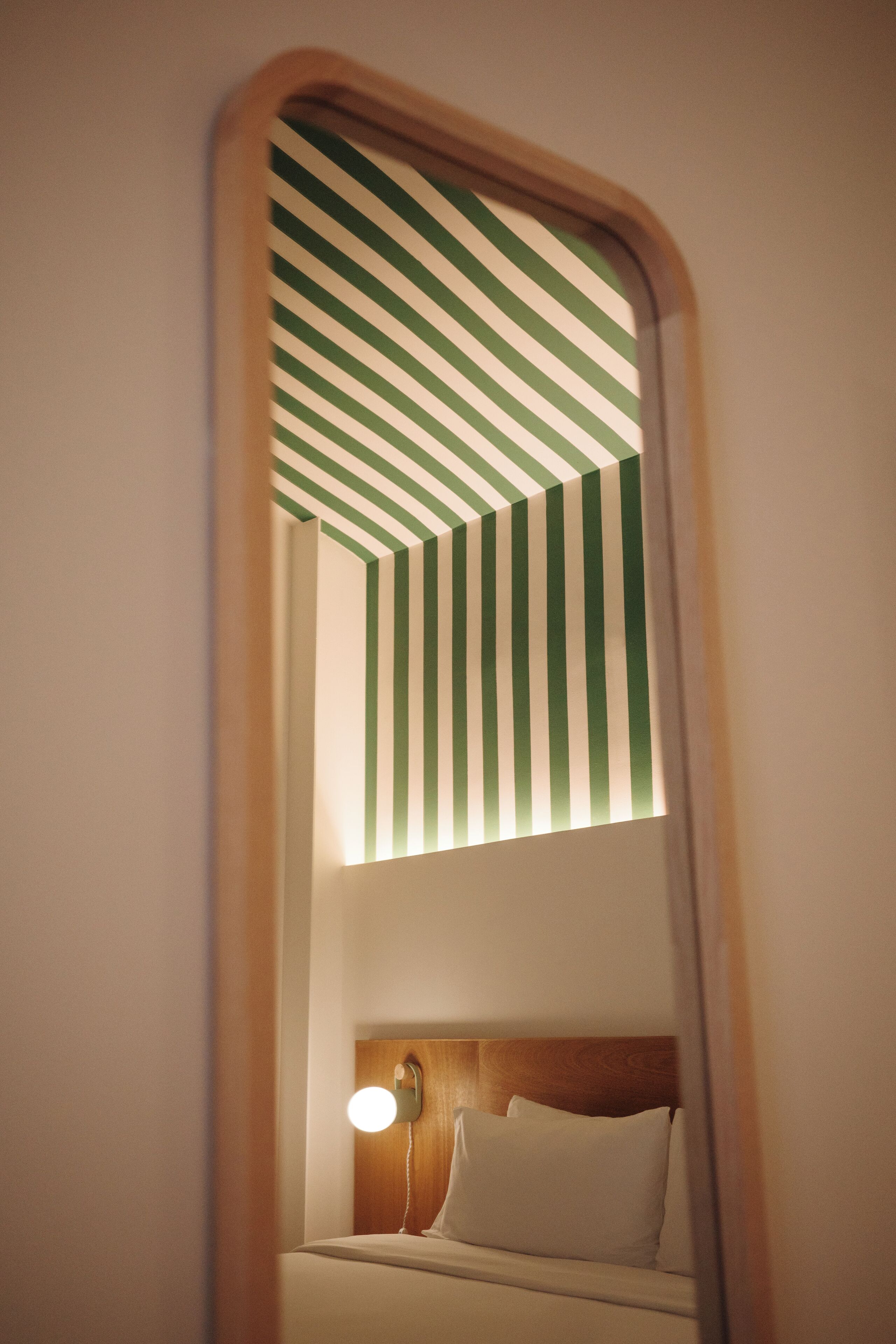Habitación de hotel con techo a rayas, cabecera de madera y lámpara de noche.