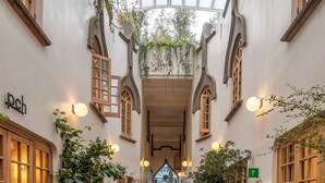 A corridor with a high ceiling, brick floor, and potted plants. - Hotel Parián (Mexico City)