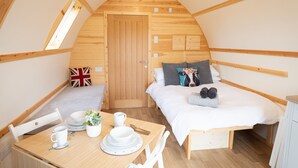 A cozy, wooden-paneled room with a bed, a small table with breakfast items, and a door with a British flag pillow. - Cosy Spacious Cabin with Wood Fired Hot Tub (Cumwhitton)