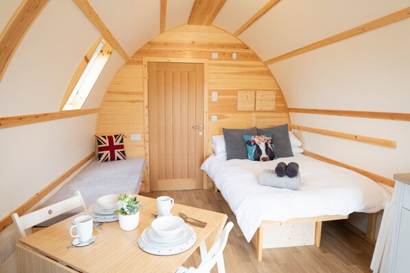 A cozy, wooden-paneled room with a bed, a small table with breakfast items, and a door with a British flag pillow.