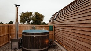 A hot tub with a wooden exterior, a metal heater, and a wooden fence. - Cosy Spacious Cabin with Wood Fired Hot Tub (Cumwhitton)