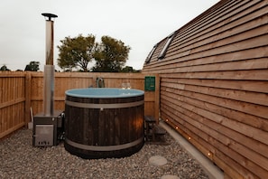 A hot tub with a wooden exterior, a metal heater, and a wooden fence.