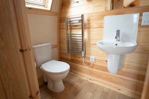 Une petite salle de bain avec des toilettes blanches, un porte-serviettes chromé et un lavabo blanc avec un pare-éclaboussures à motifs.