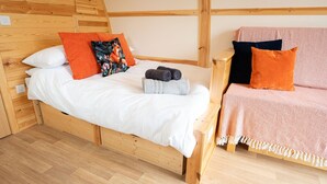 Un lit en bois avec une literie blanche et des coussins orange, une petite table de chevet en bois et un canapé rose avec une couverture.