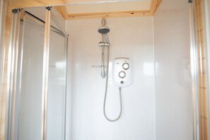 Un petit espace douche fermé, équipé d’un pommeau de douche à main et d’un panneau de commande.