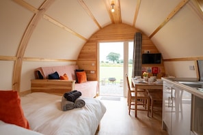 Une pièce chaleureuse, avec des murs en bois, comprenant un lit, un bureau et un coin cuisine.