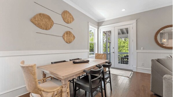 Un comedor con mesa y sillas de madera, un adorno de pared tejido y vistas a través de un ventanal.