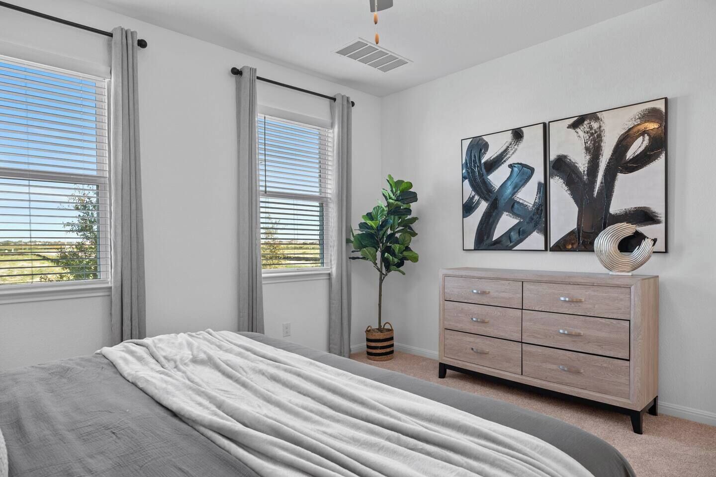 Een slaapkamer met een bed, een dressoir, een potplant en abstracte kunst aan de muur.