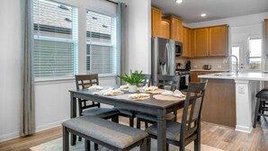 A modern kitchen with wooden cabinets, a stainless steel refrigerator, and a dining area with a table set for four.