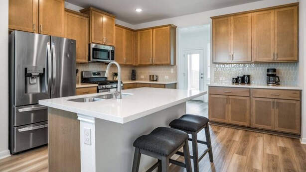 A modern kitchen with wooden cabinets, stainless steel appliances, a large island with stools, and a tiled backsplash.