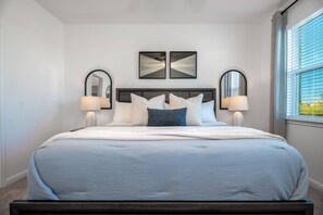 A bedroom with a large bed, two wall-mounted mirrors, and a window with blinds.
