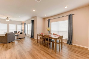 A modern living room with a sofa, a dining table with chairs, and a ceiling fan.