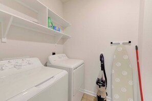 A laundry room with a washing machine, dryer, shelves with detergent, and a vacuum cleaner.
