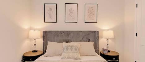 A neatly arranged bedroom with a large bed, two bedside tables, and three framed botanical illustrations on the wall.