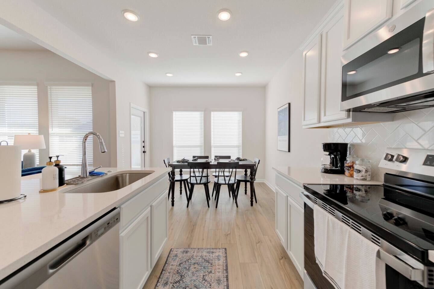 A modern kitchen with white cabinetry, a dining area with a table and chairs, and a built-in oven.