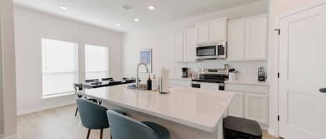 A modern kitchen with white cabinetry, a central island with bar stools, a microwave, and an oven.