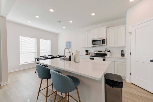 A modern kitchen with white cabinetry, a central island with bar stools, a microwave, and an oven.