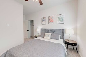 A bedroom with a bed, two bedside tables, a ceiling fan, and three framed artworks on the wall.