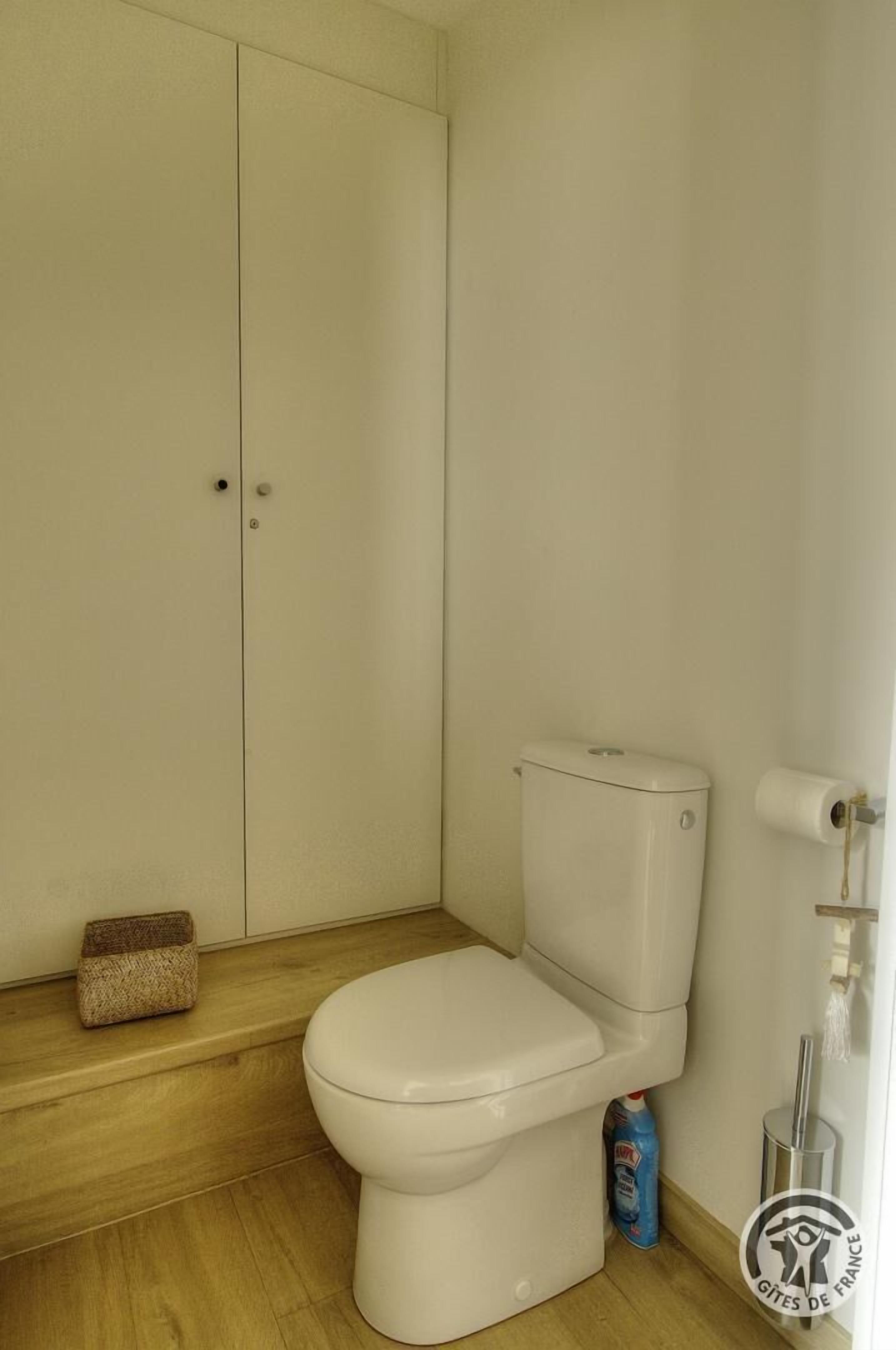 Une petite salle de bain propre, avec des toilettes, un plancher en bois et un meuble de rangement.