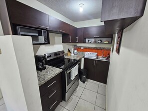 A compact kitchen with dark cabinets, a microwave, stove, and a sink. - Cozy apartment in the Heart of San Salvador with 3 bedrooms and parking free. (San Salvador)