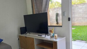 A modern living room with a flat-screen TV on a white console, a small statue, and a remote control.
