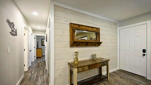 A hallway with wooden flooring, a wooden console table with a mirror above it, and a white door on the right. - Diamond in the Ruff -4bdrm Hot Tub / Firepit / Boat Parking Broken Bow Hochatown (Broken Bow)