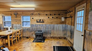 A rustic cabin interior with wooden walls, a dining table, chairs, a fireplace, and a window. - 1-bedroom cabin in Redfield (Redfield)