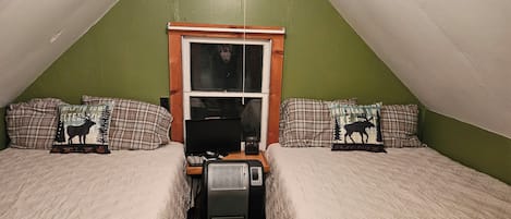 Camera da letto mansardata con soffitto spiovente, una finestra e biancheria a quadri.