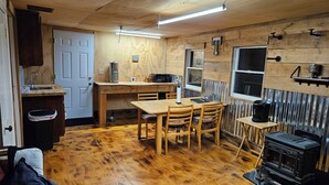 A rustic kitchen with wooden walls, a dining table, chairs, a stove, and a window. - 1-bedroom cabin in Redfield (Redfield)