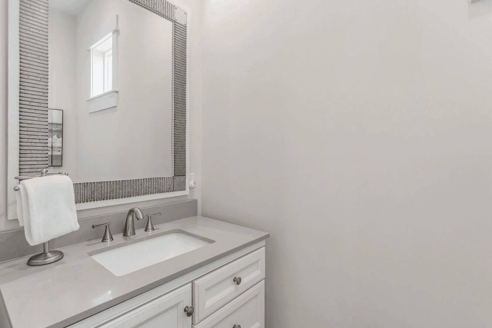 A modern bathroom with a white sink, a mirror, and a towel hanging on the wall.