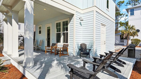 A house with a covered porch, outdoor seating, and a grill.