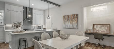 A modern kitchen with white cabinets, a central island, and a dining area with a white table and chairs.