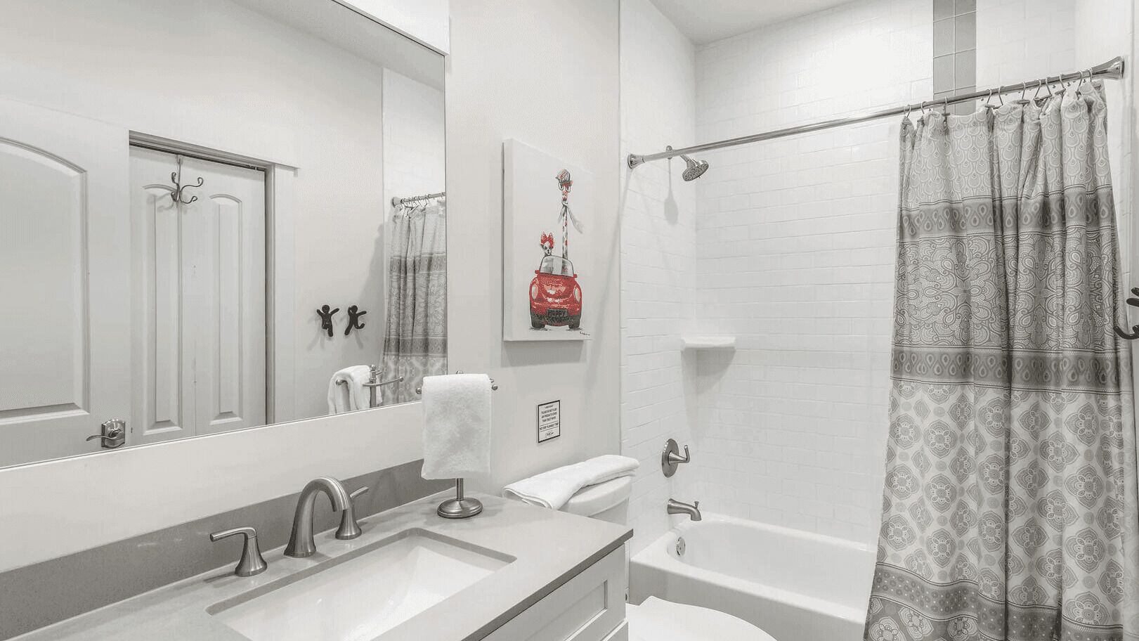 A modern bathroom with a large mirror, a sink, a toilet, and a shower.
