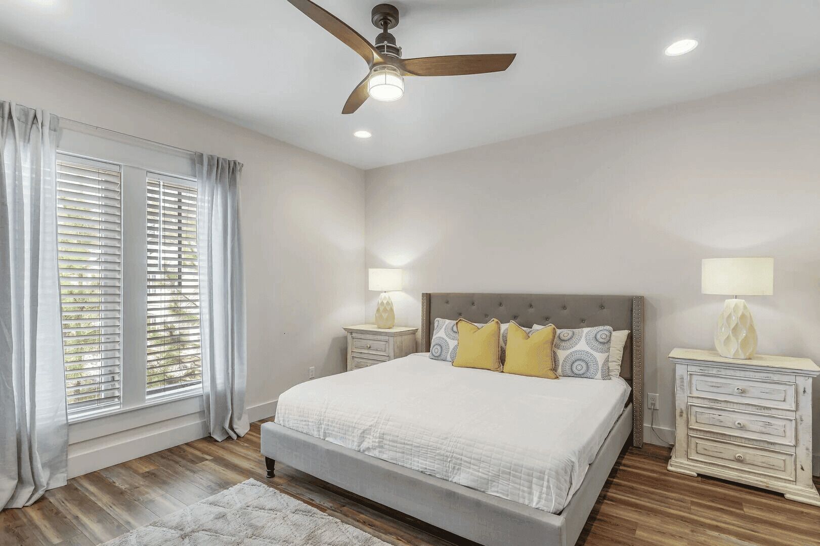 A bedroom with a bed, curtains, a ceiling fan, and bedside lamps.