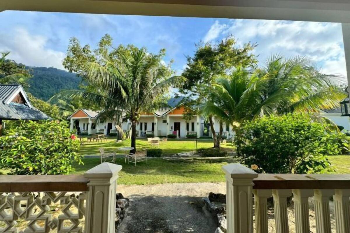 Vista de un resort con un camino pavimentado que lleva a un edificio de techo rojo, rodeado de palmeras y follaje.