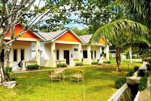 A row of single-story buildings with a flat roof, a grassy lawn, and a palm tree. - Dreamz Village (Langkawi)
