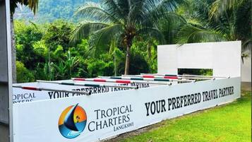 A white sign with 'Tropical Charters Langkawi' and 'Your Preferred Travel Partner' text, set against a backdrop of greenery and palm trees.
