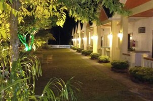 Un patio de hotel por la noche con senderos iluminados y una hilera de habitaciones a un lado.